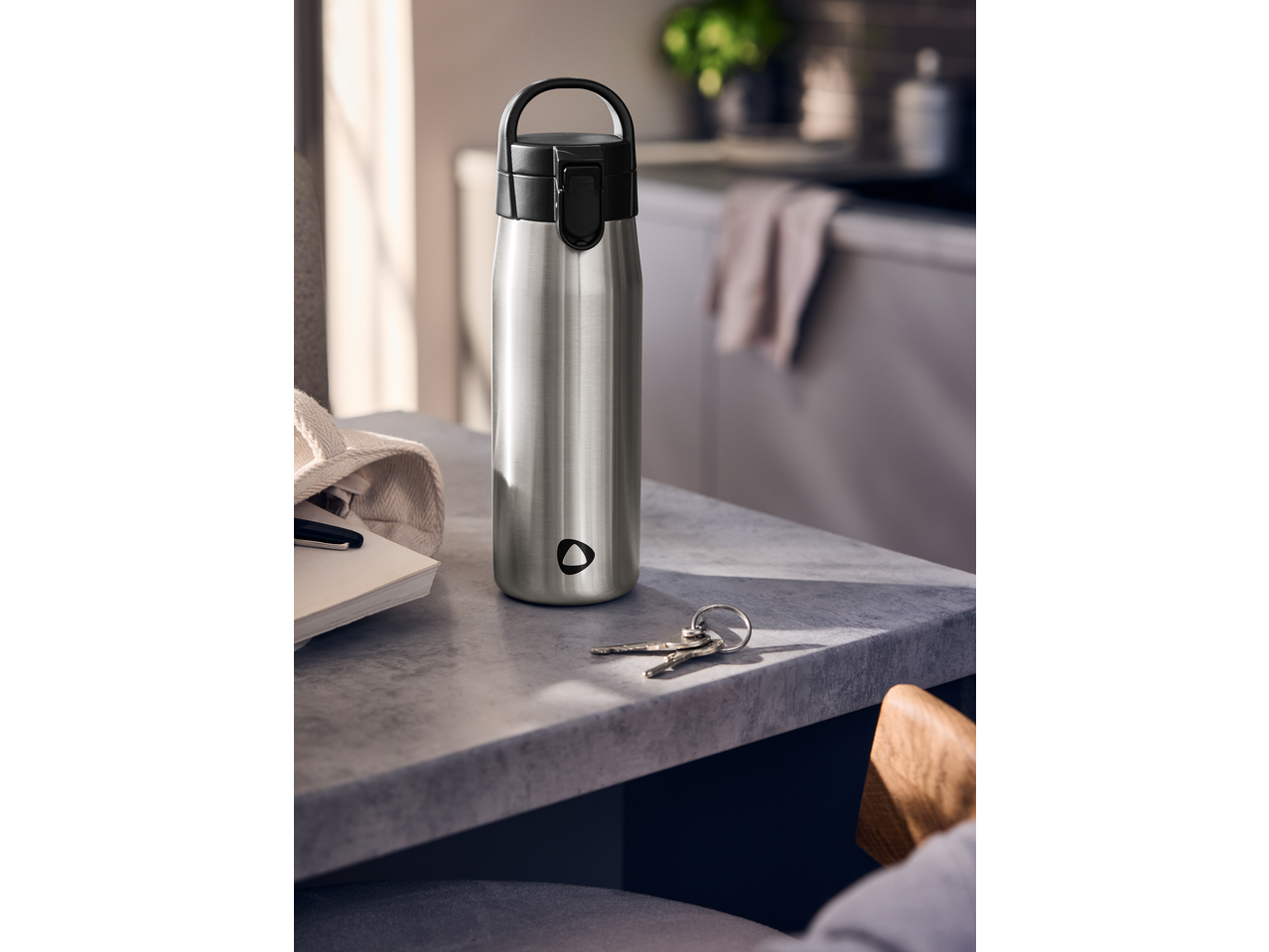 Garrafa Silvercrest de aço inoxidável numa mesa com chaves e um caderno.