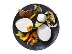 Coconut dessert with fresh fruit, coconut flakes, and mint on a dark plate.