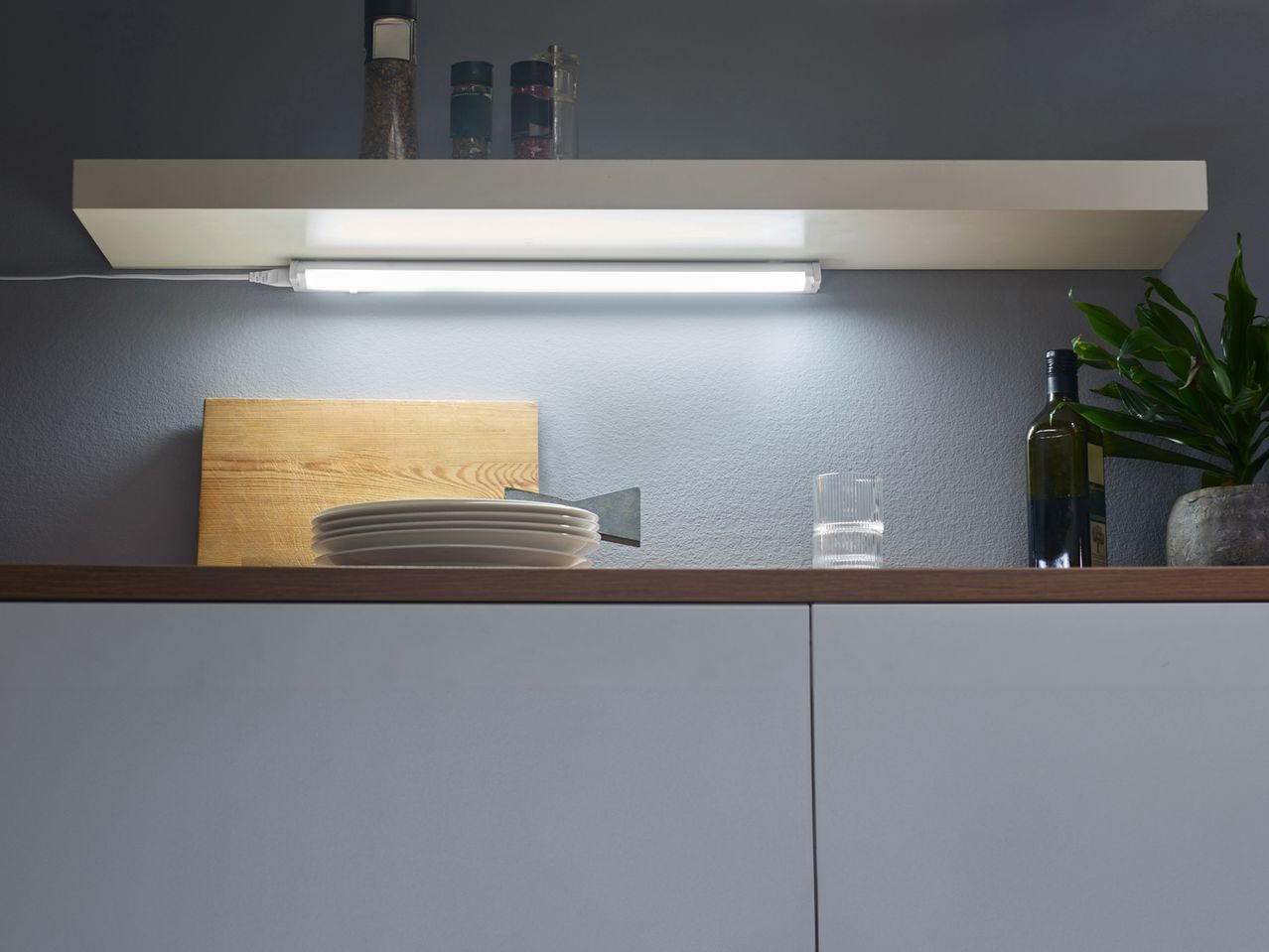 Kitchen shelf with under-cabinet lighting, spices, cutting board, and dishes.