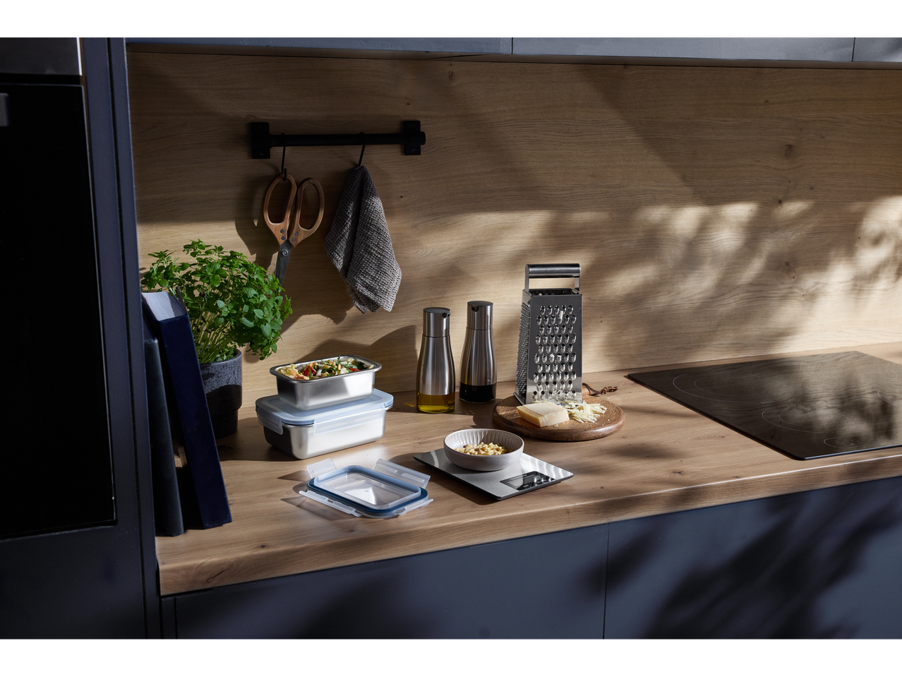 Cântar digital de bucătărie cu un bol de semințe de pin, răzătoare de brânză și recipiente pentru alimente pe un blat de lemn.