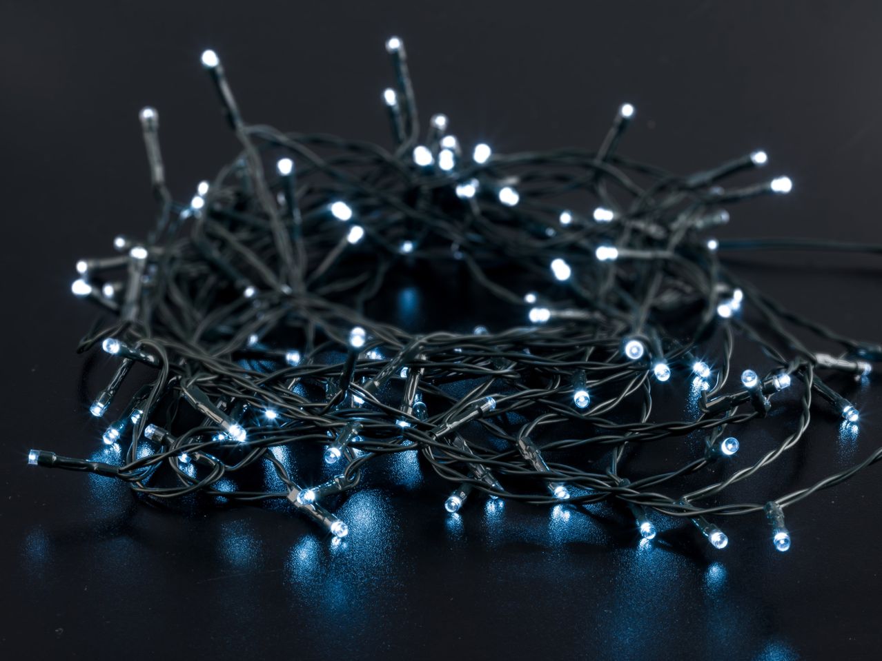 Close-up of white LED Christmas lights tangled on a dark surface, emitting a cool glow.