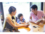 A family playing UNO card game together, smiling and laughing around a wooden table.