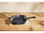 Tigaie grill din fontă pe un tocător de lemn cu ciuperci și ceapă verde.