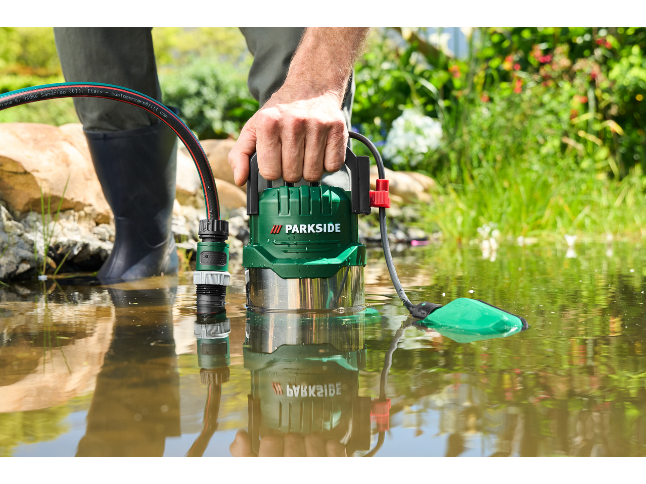 Man using a green PARKSIDE submersible pump for clear/dirty water in a pond.