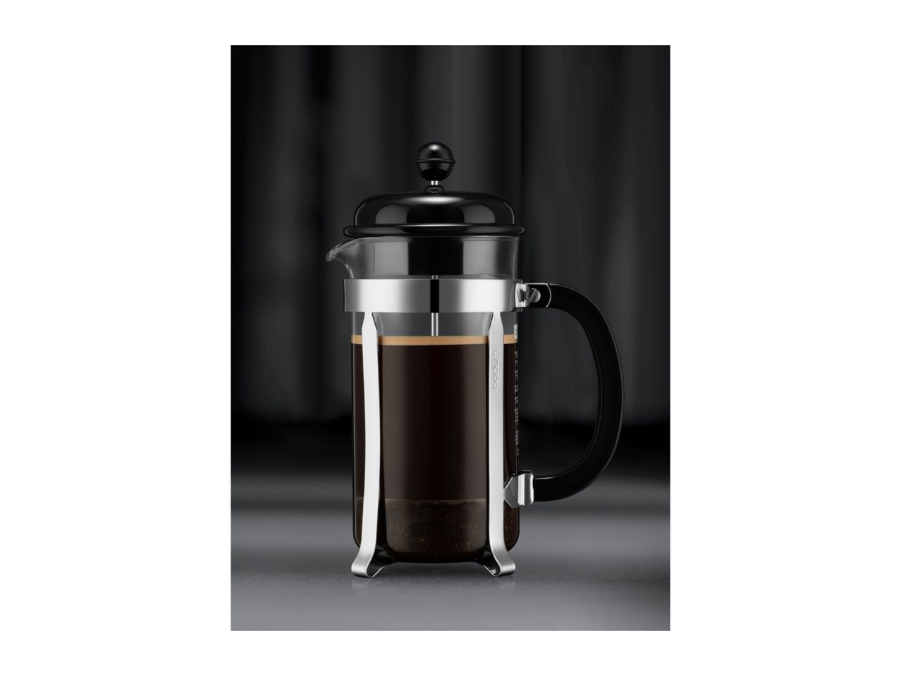 A classic glass French press filled with freshly brewed coffee on a dark background.