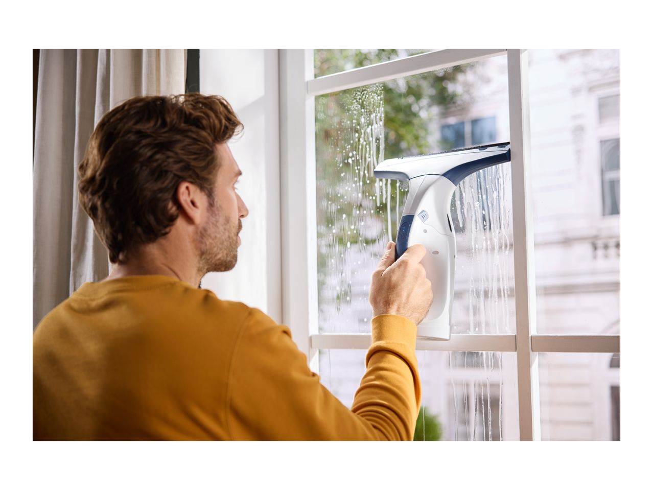 Man cleaning a window with a window vacuum cleaner, leaving streaks of foam.