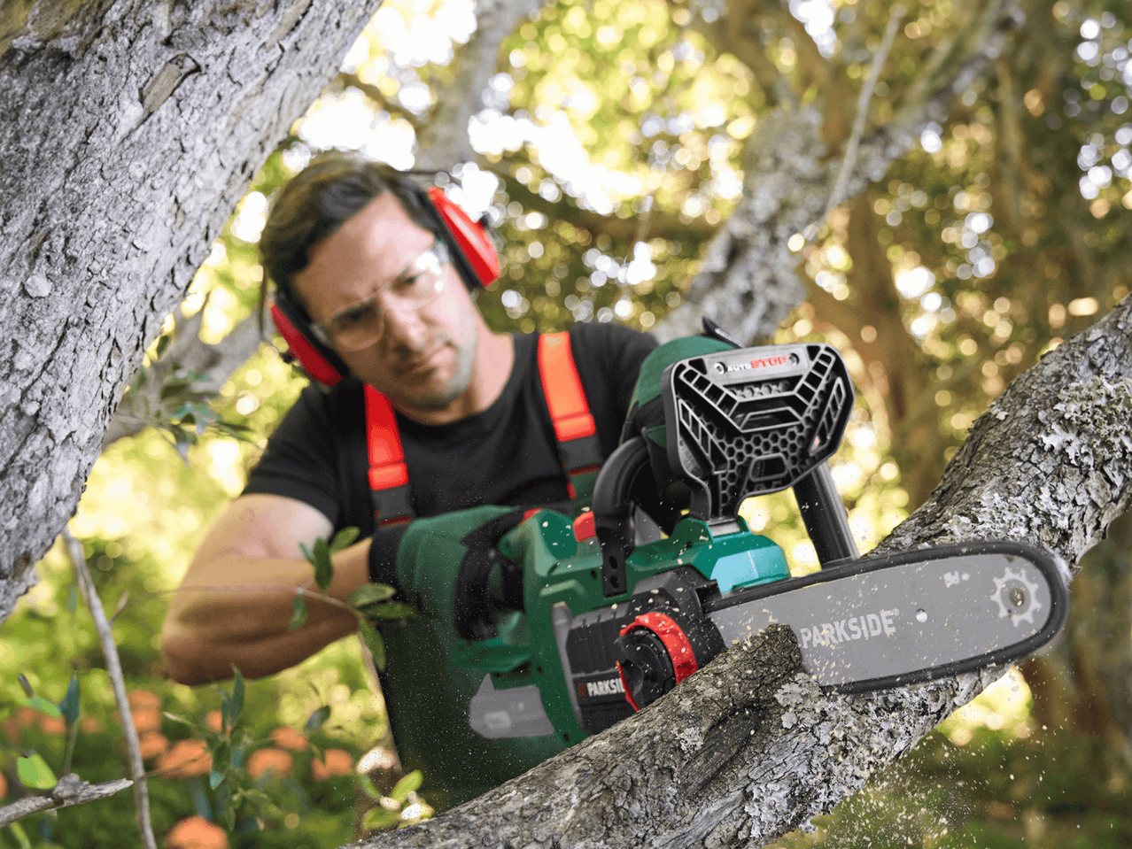 Mann mit Gehörschutz und Schutzbrille schneidet mit einer Kettensäge einen Ast ab.