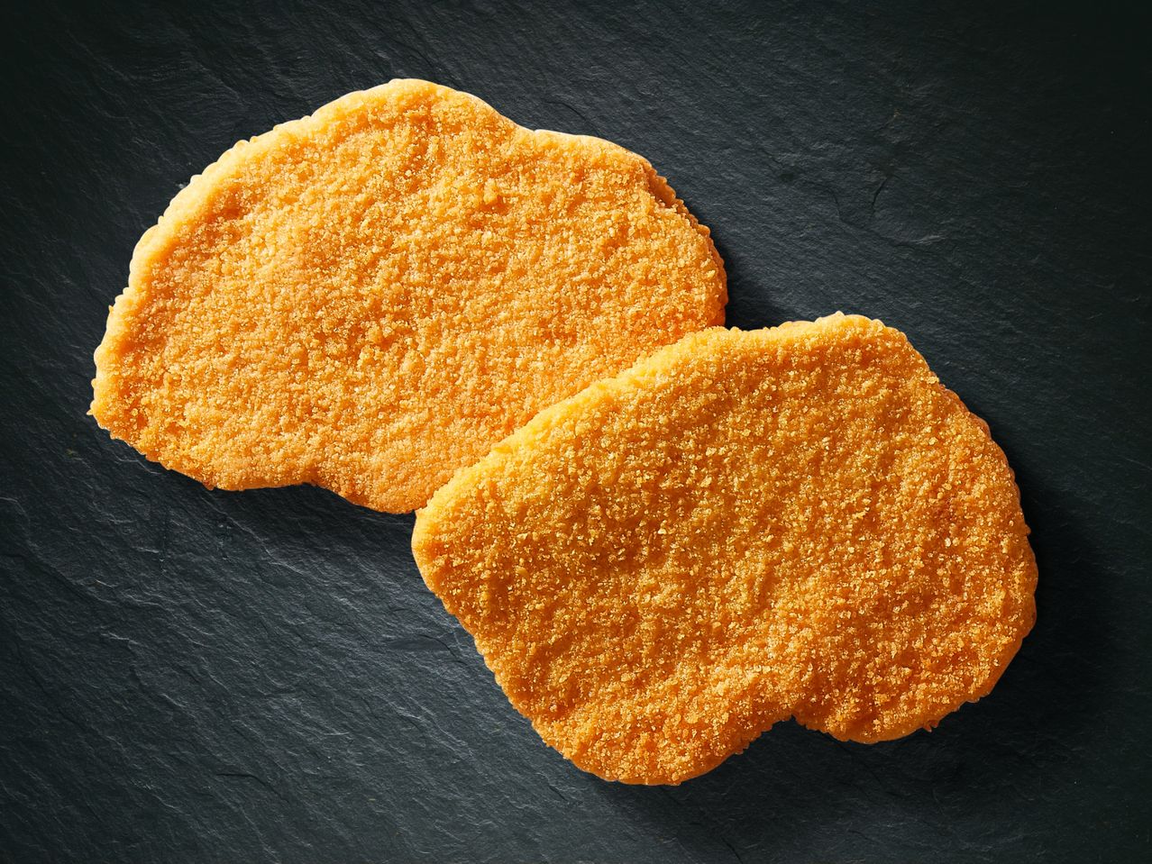 Zwei panierte Schnitzel auf dunklem Untergrund.