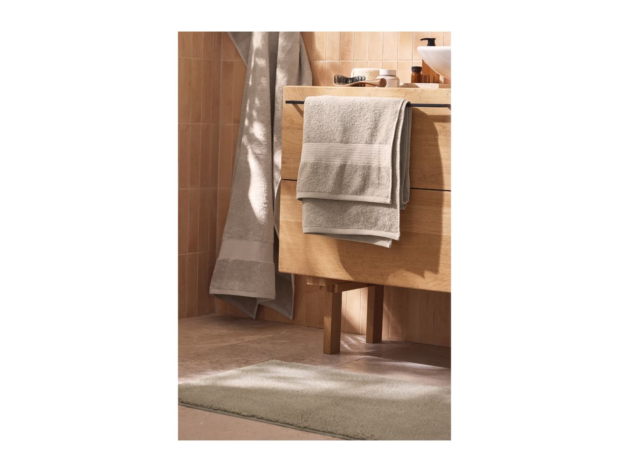 Bathroom with beige towels, a wooden vanity, and a light green bath mat.