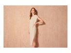Woman in a light beige midi dress with a side knot detail and green hoop earrings.