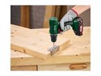 A person wearing work gloves uses a cordless drill to attach a hinge to a wooden board.