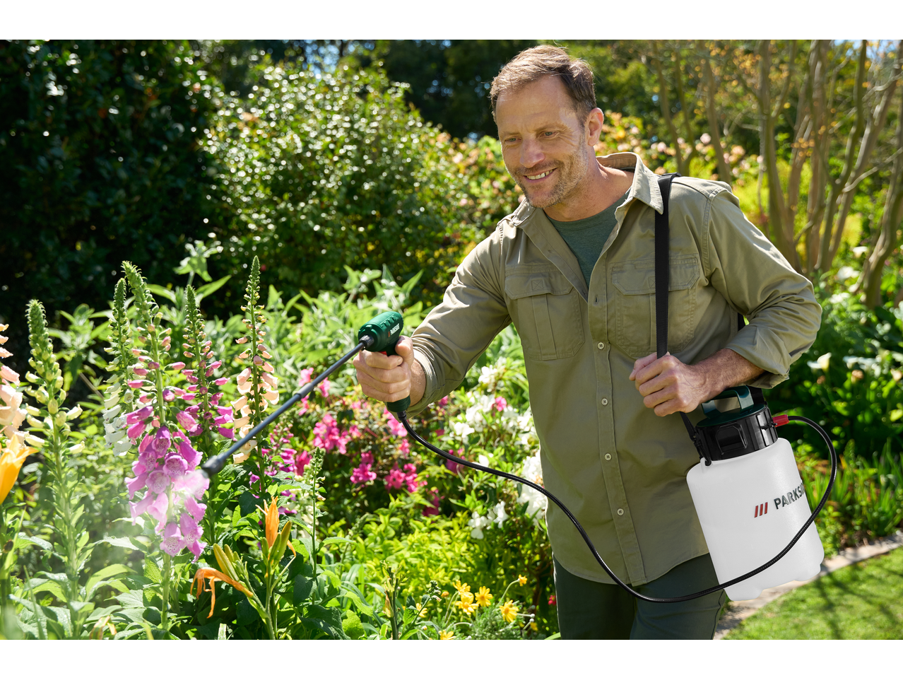 Man using a Parkside 4V Cordless Pressure Sprayer on flowers in a garden.