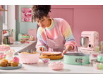 Woman decorating cakes with SILVERCREST® Cake Tin Assortment, pink mixer, and colorful sweets.