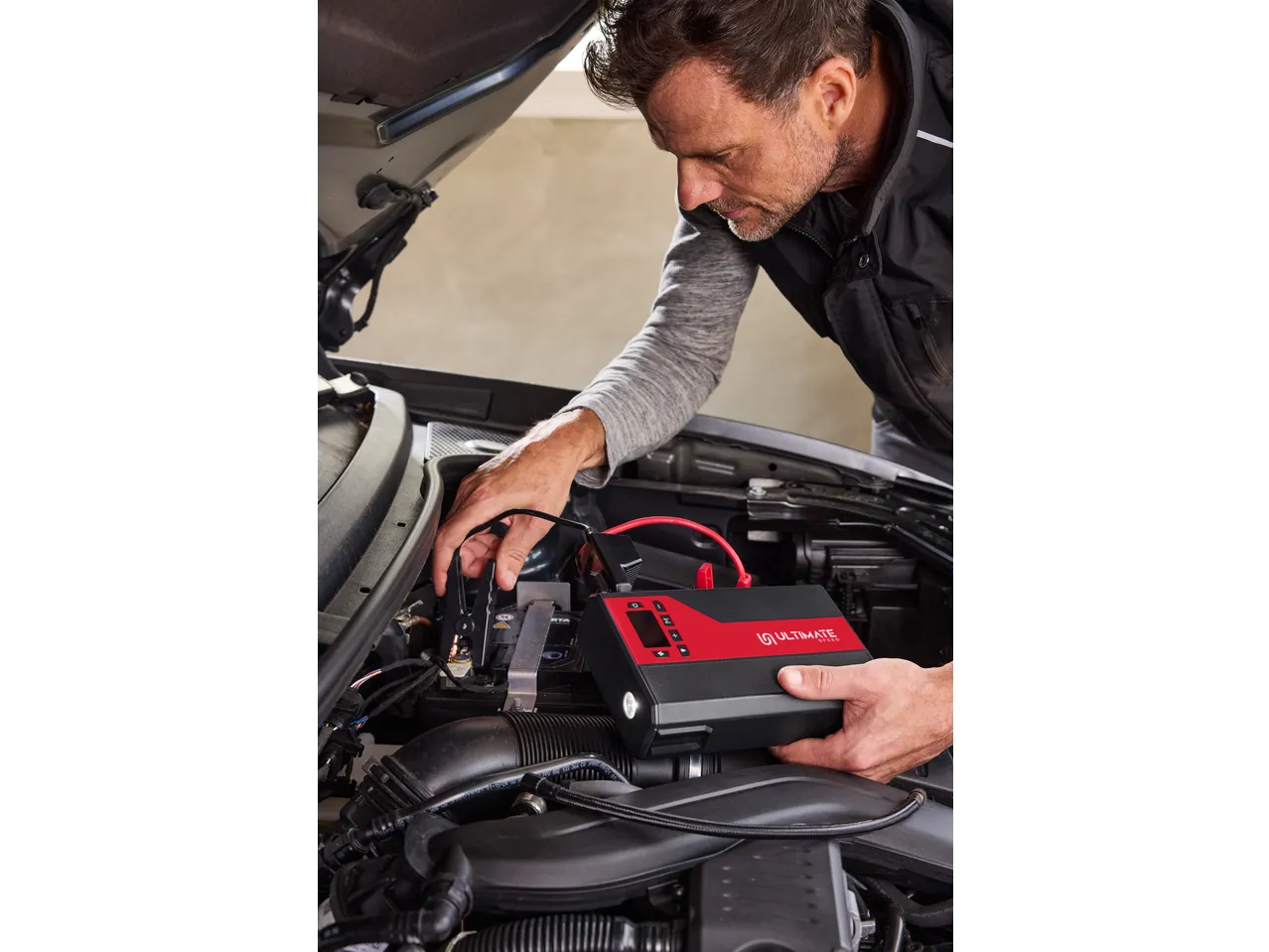 Man jump-starting a car with a portable jump starter, connecting cables to the car battery.