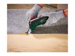Hands in protective gloves using a multi-tool to remove flooring from a wooden surface.