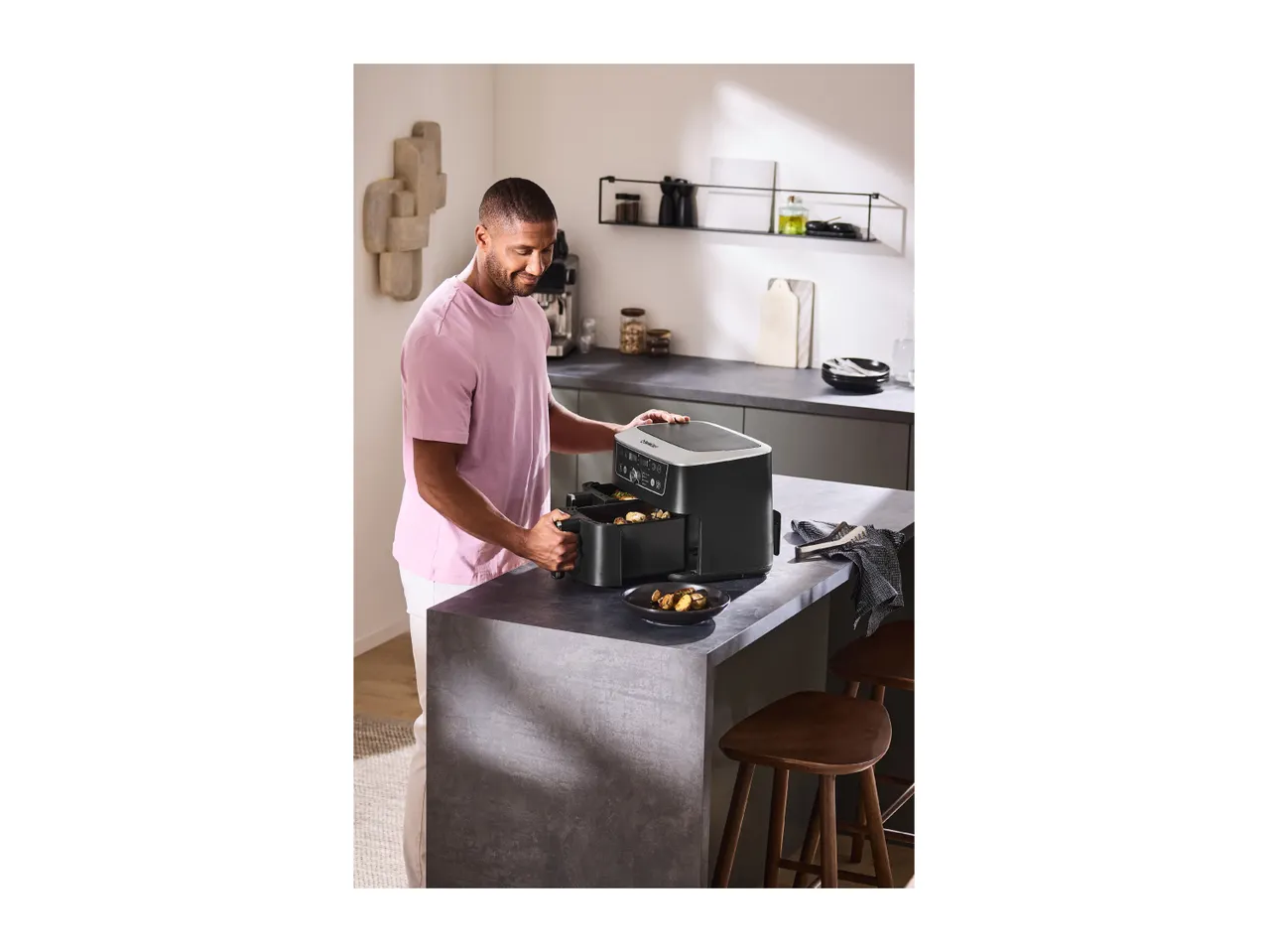Man in a modern kitchen using a dual-basket air fryer to cook food.