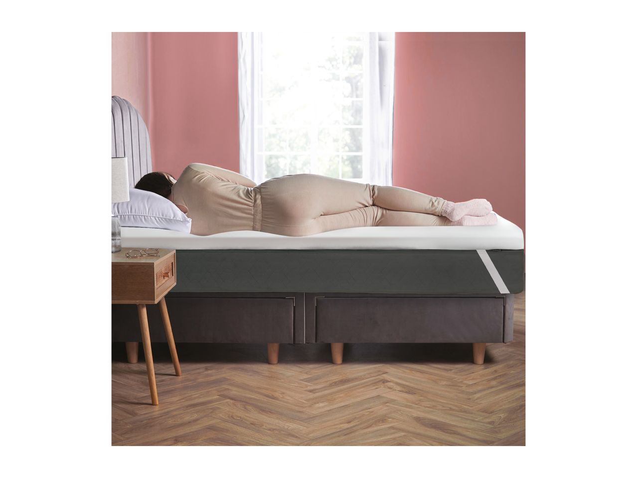 Woman sleeping on a dark grey mattress with a white top layer, next to a wooden nightstand.