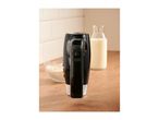 Black hand mixer standing on a wooden countertop next to a bowl of flour and milk