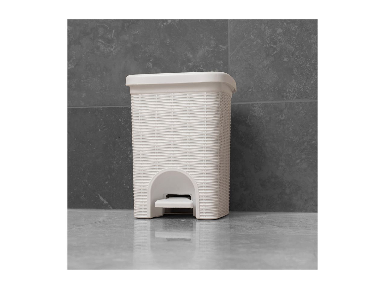 A white plastic step-on trash can sits on a gray floor.