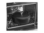 Black cast iron pot with lid inside an oven on a metal rack.