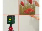 Un laser cu linii încrucișate proiectează linii roșii pe un perete în timp ce se agață un tablou.
