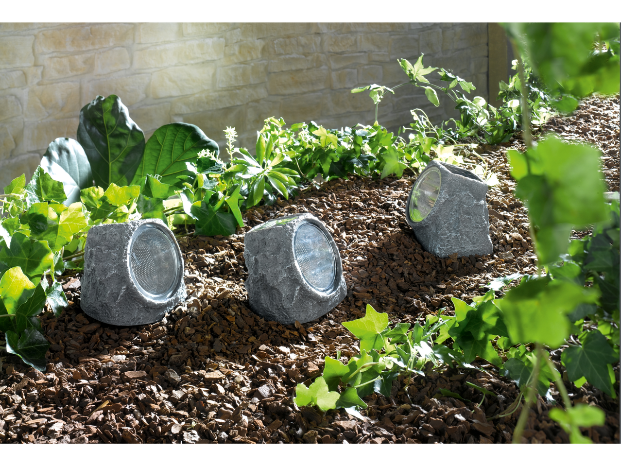 Three solar-powered rock lights nestled in mulch and greenery.