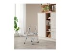 A silver step stool stands on a tiled floor in a room with a cabinet and a plant.