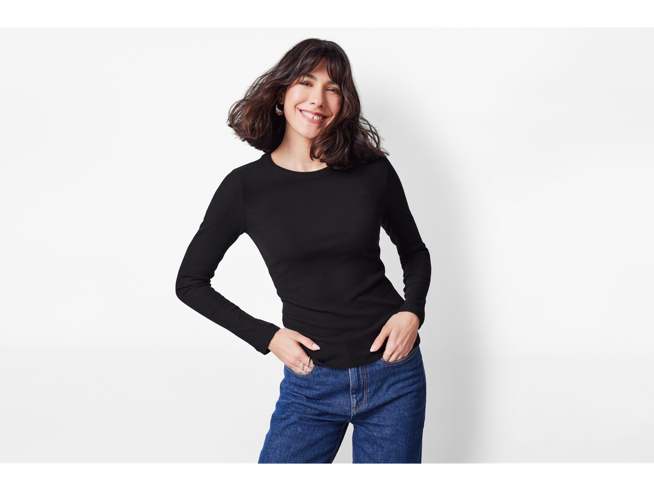 Nasmijana žena u crnoj majici dugih rukava esmara® i plavim trapericama.