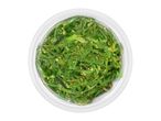 Overhead view of a clear plastic container filled with vibrant green seaweed salad, sprinkled with sesame seeds.