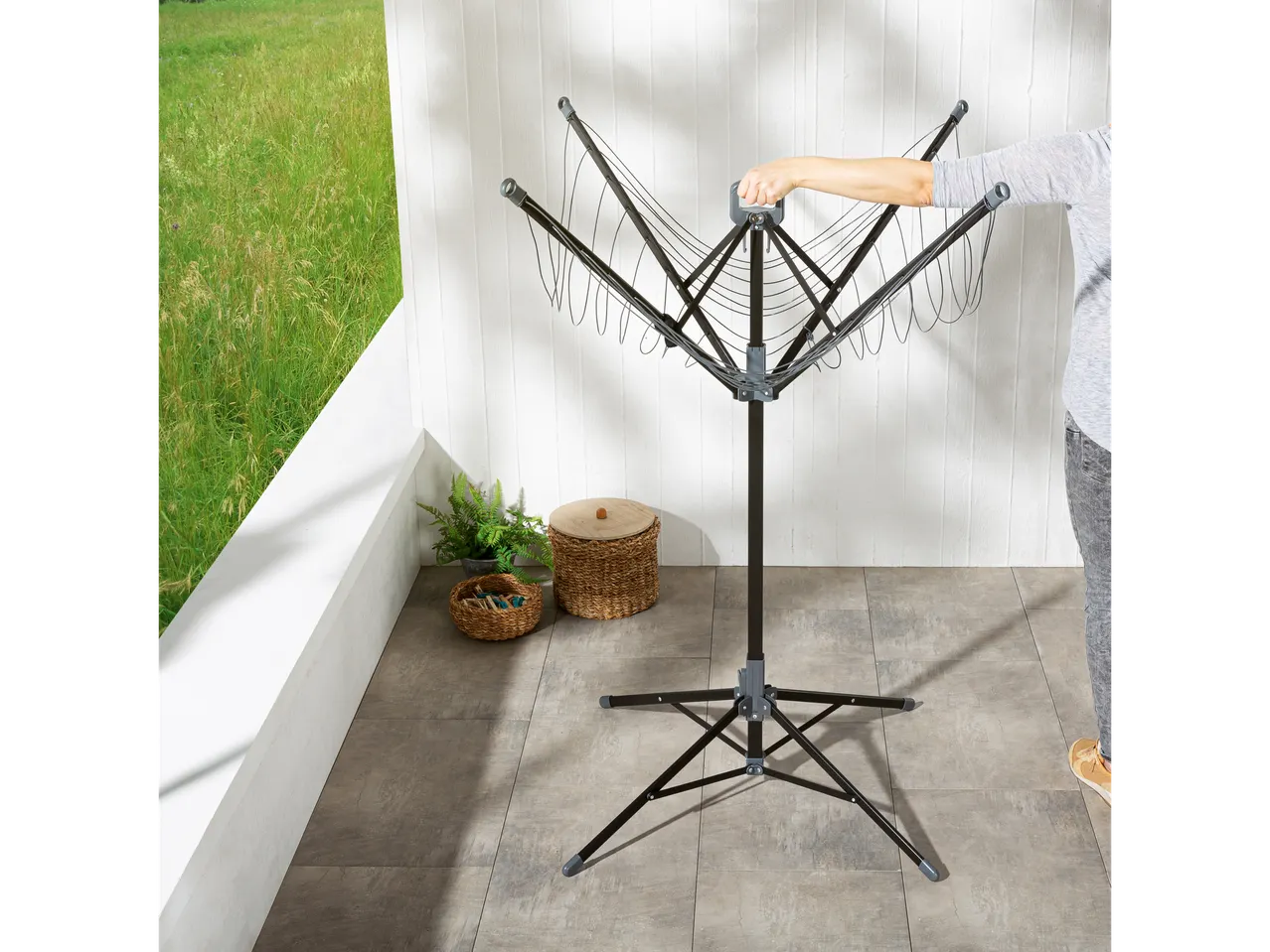 A person opens a black, foldable laundry drying rack with multiple lines on a patio.