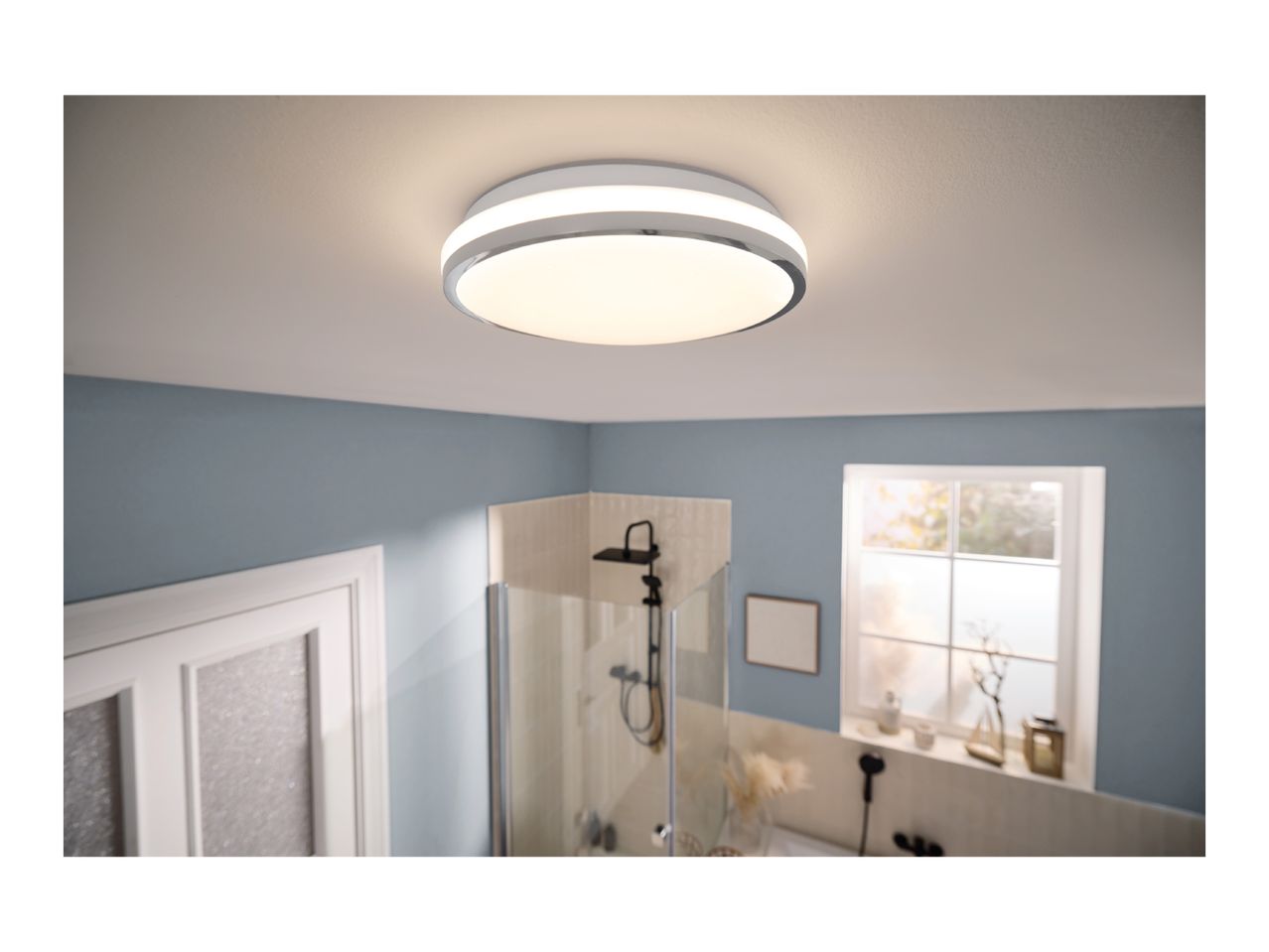 Modern LED ceiling light illuminating a bathroom with a shower and window.