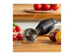 Hand blender with tomatoes and salt on a wooden board, with a bowl of soup in the background.