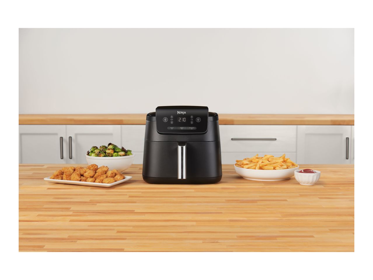 Black air fryer on a wooden counter with chicken nuggets, brussels sprouts, and fries.