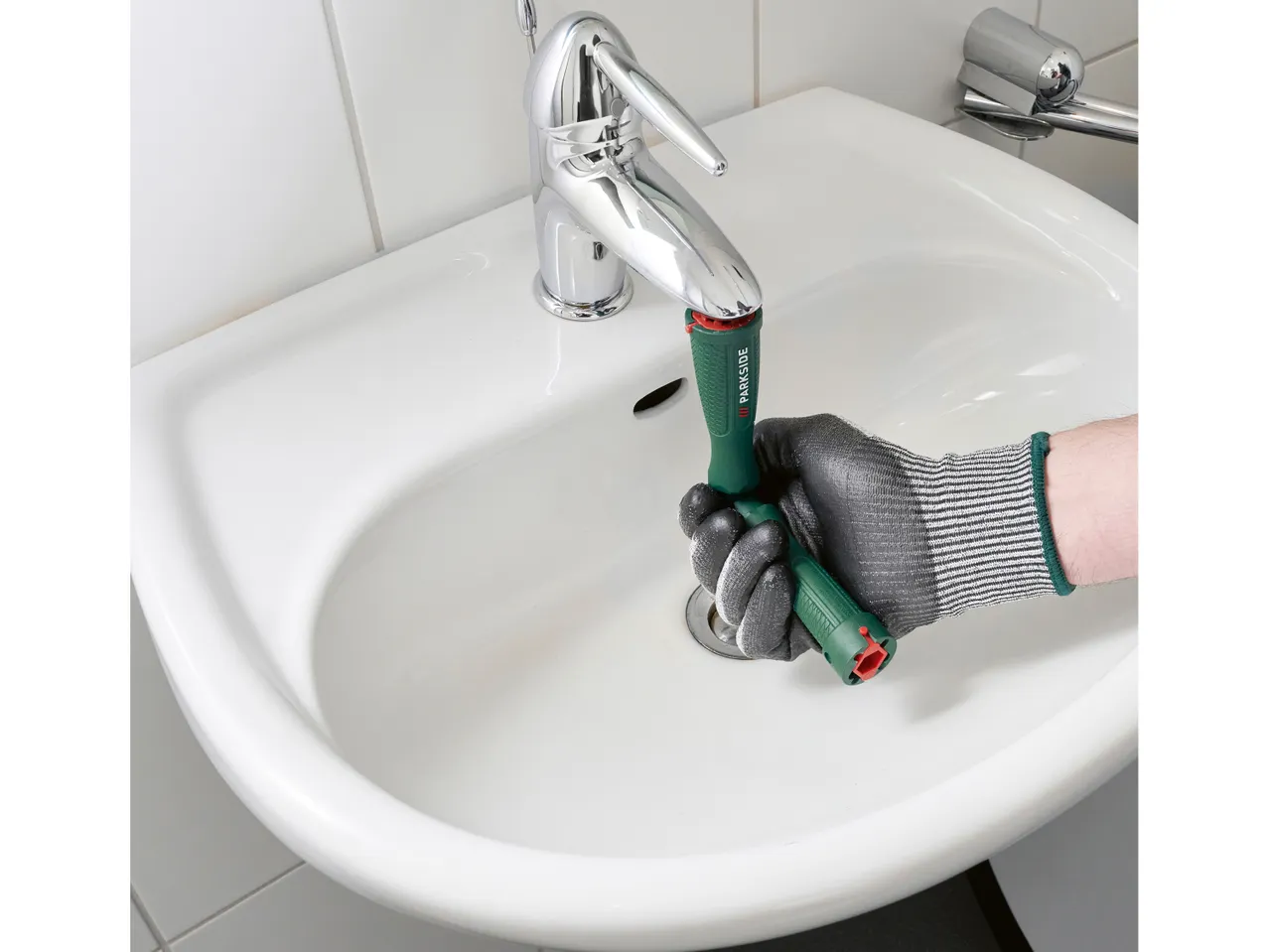 Una mano guantata usa un attrezzo verde per la manutenzione del lavandino.