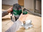 A person using a Parkside® 1200W Router to cut a curved groove in a wooden surface.