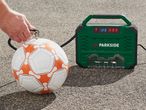 A person inflating a white and orange football with a green portable air compressor.