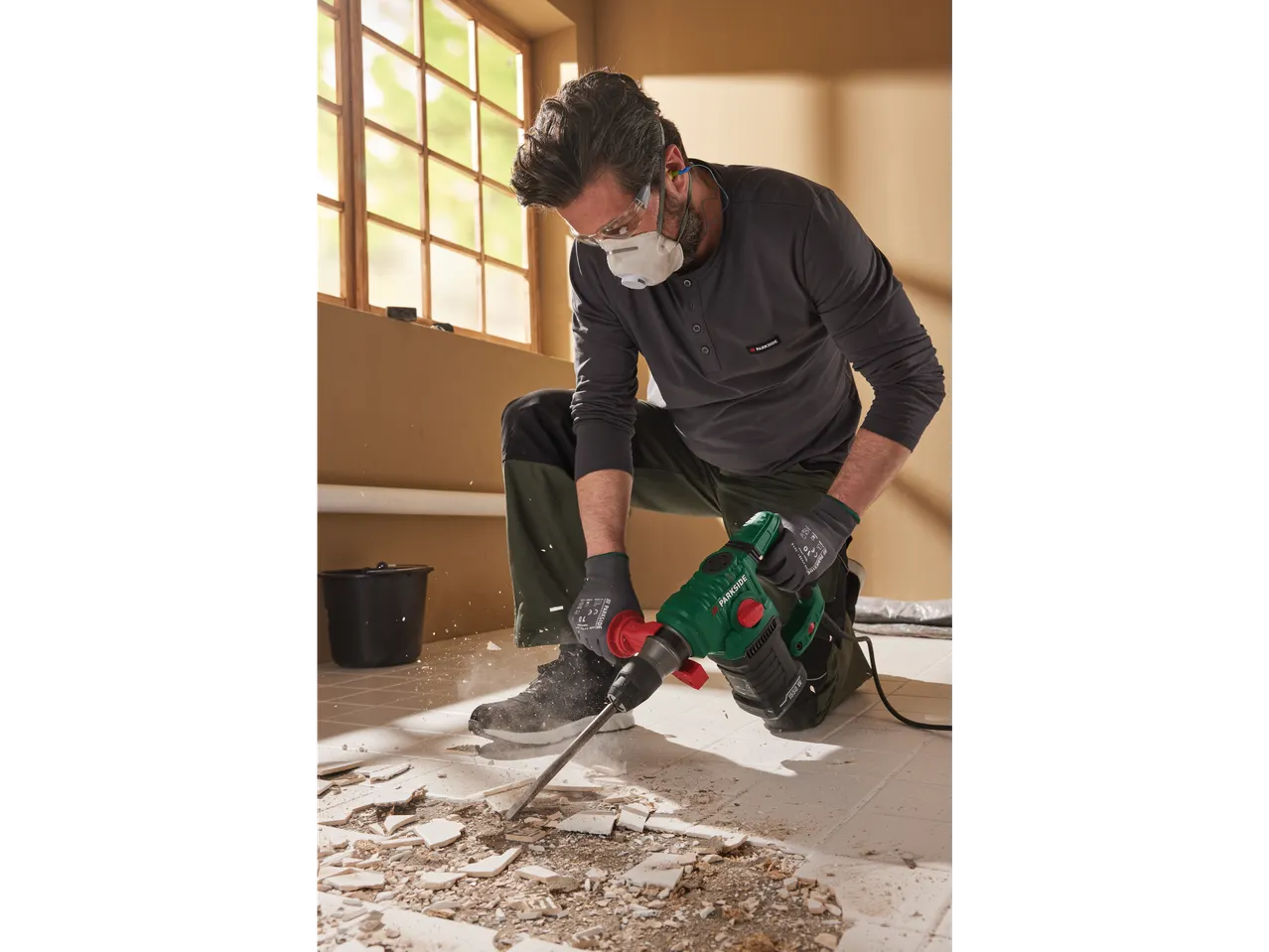 A man uses a Parkside 1650W demolition hammer to remove floor tiles.
