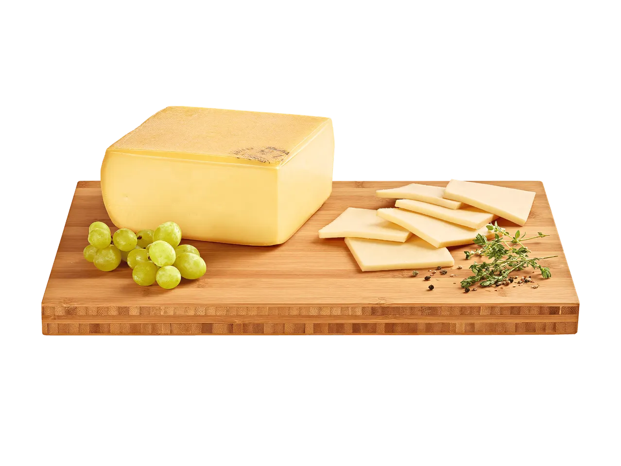 Ein Block Käse mit Scheiben, Weintrauben und Kräutern auf einem Holzbrett.