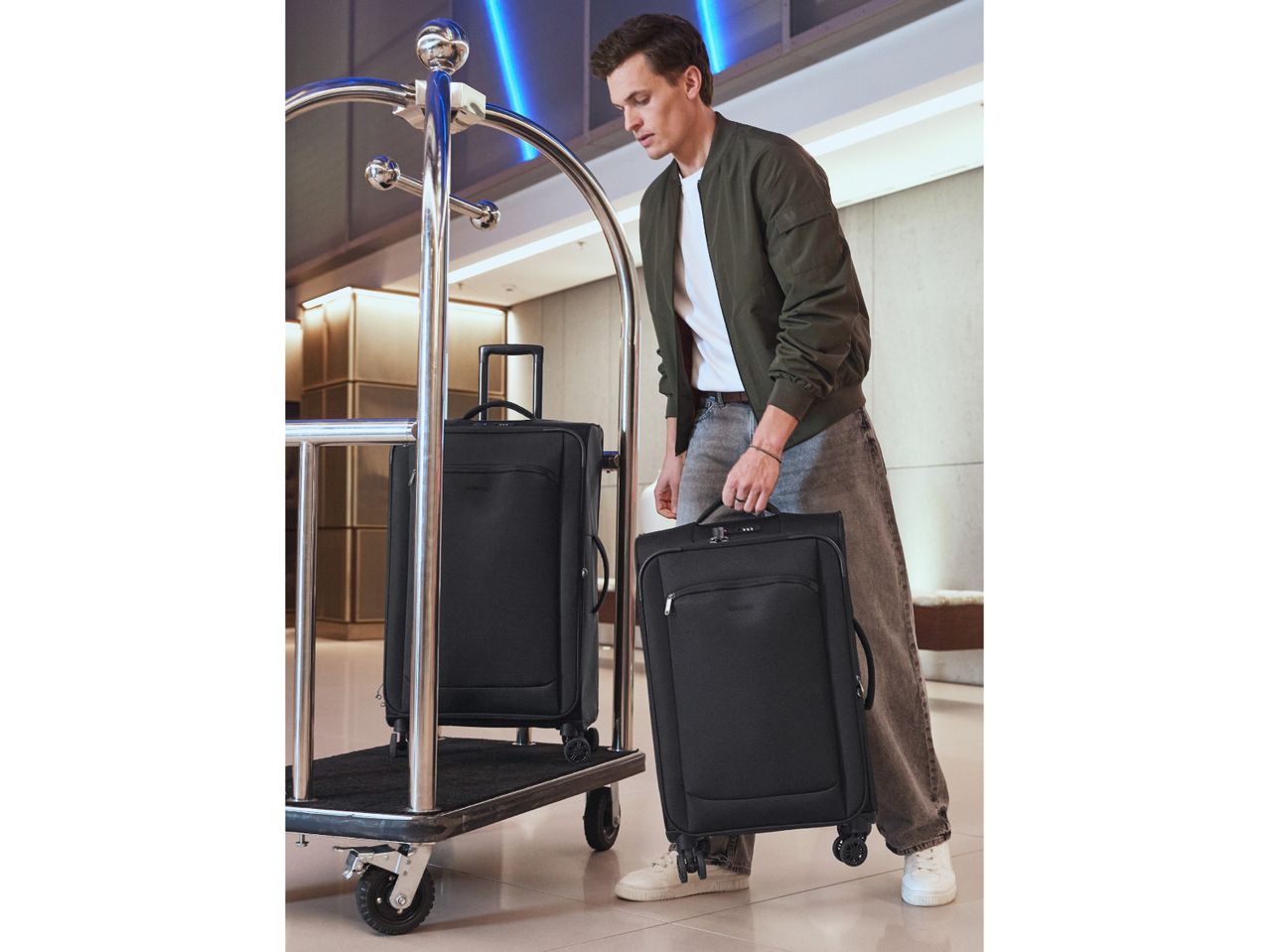 Man in a hotel lobby placing a black suitcase on a luggage cart.
