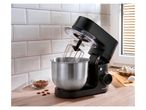 Black stand mixer with a stainless steel bowl, next to almonds and eggs.