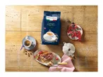 A bag of espresso coffee, a cup of coffee, tiramisu, berries, and a moka pot on a wooden table.