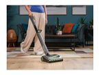 A person using a cordless floor cleaner on a wooden floor in a living room.