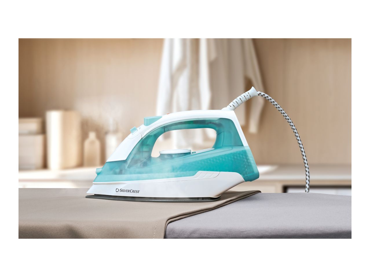 Steam iron with a turquoise water tank on an ironing board, with steam rising.