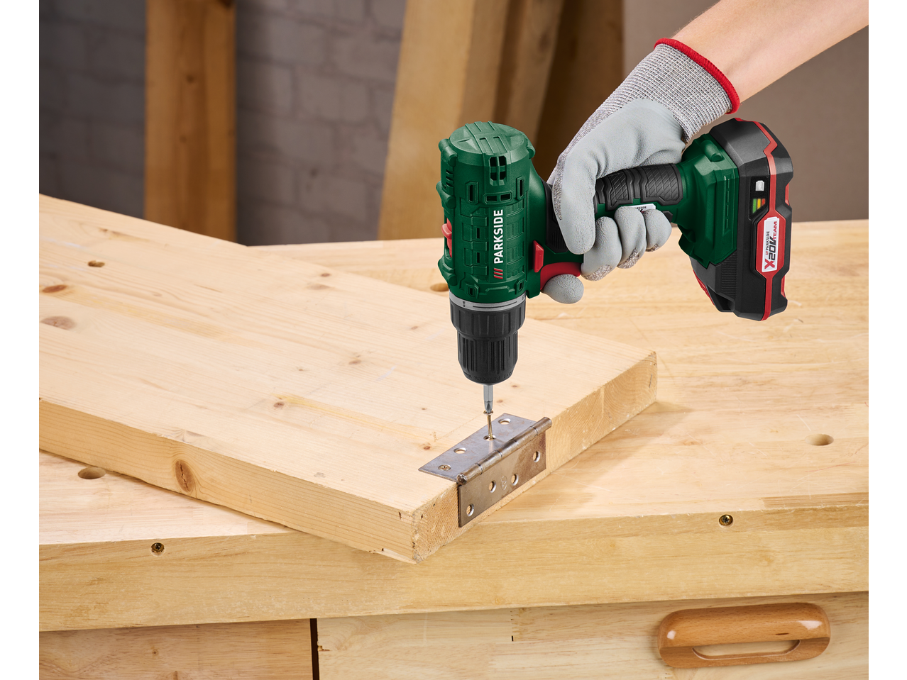 Mașină de înșurubat cu acumulator, înșurubând o balama pe o scândură de lemn.