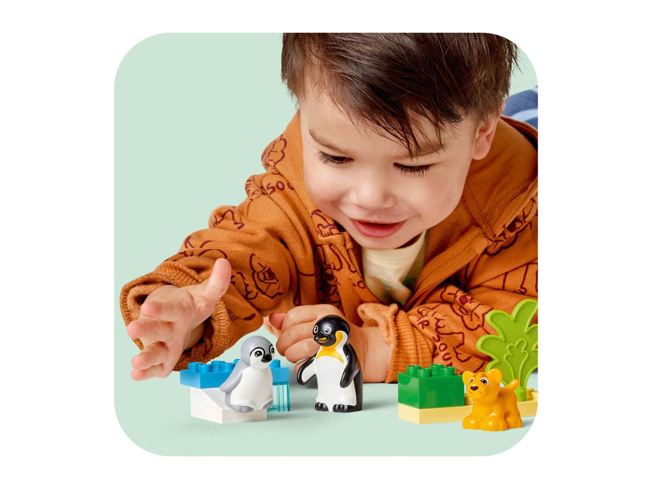 A child playing with toy penguins and a lion cub on a light green surface.