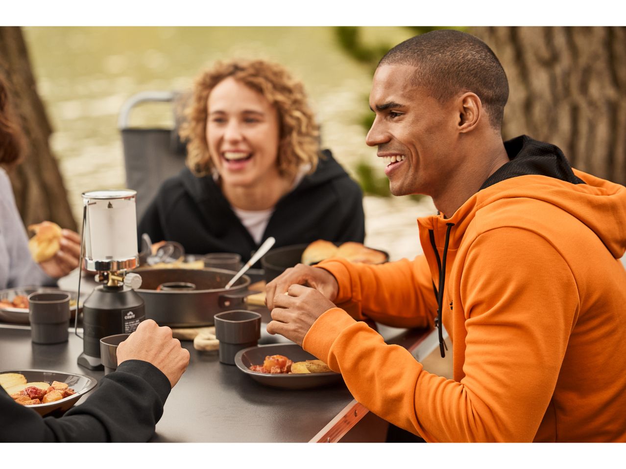 Friends enjoy a meal outdoors, wearing comfortable hoodies and using a Camping Tableware Set.