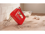 A red hand mixer with beaters and dough hooks on a wooden counter with baking ingredients.