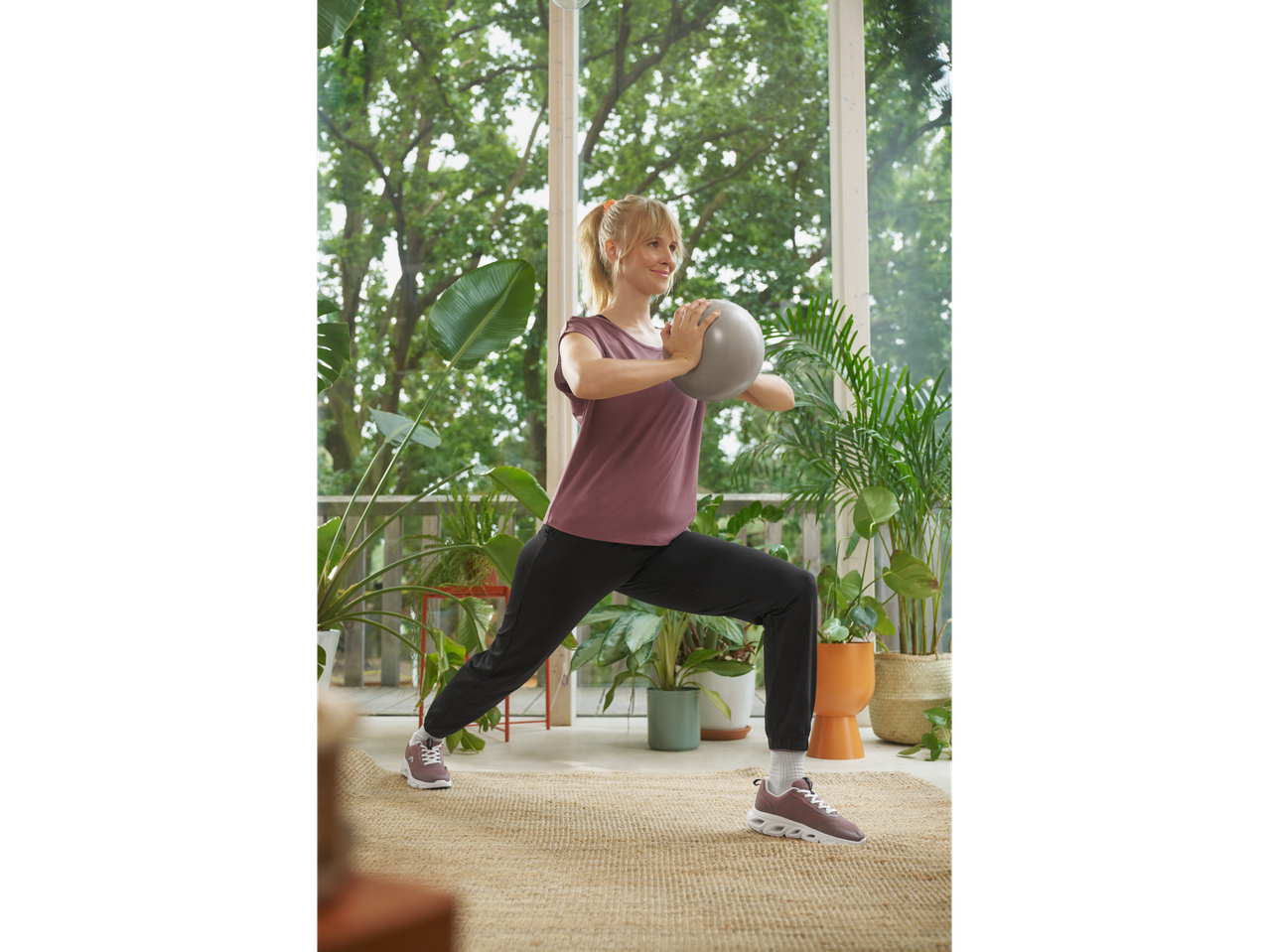 Woman in CRIVIT trainers and activewear doing lunges with a small ball.