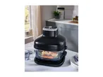 A black air fryer with cooked salmon and vegetables inside, on a kitchen table.