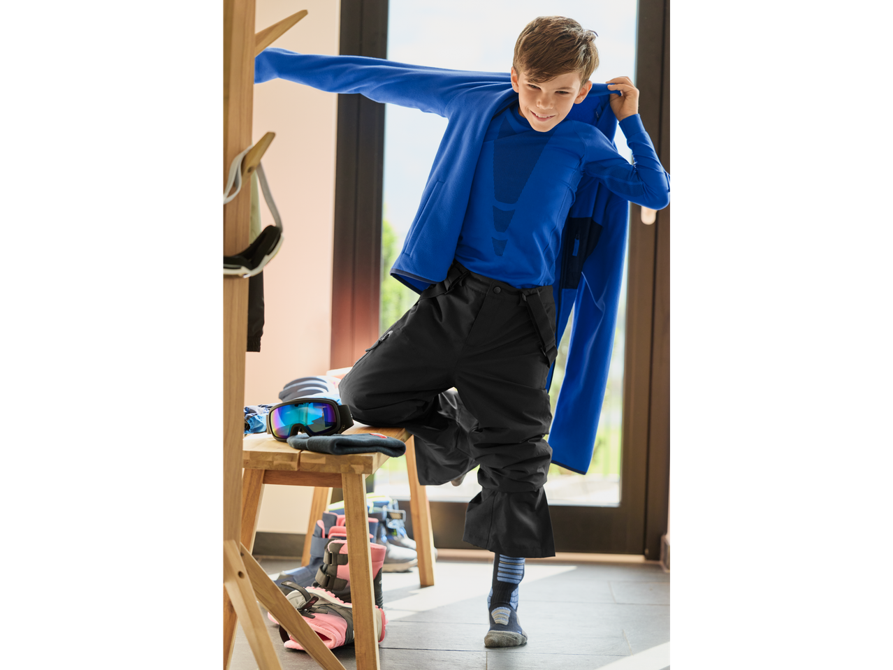 Boy wearing CRIVIT Kids' Seamless Base Layer Set and ski pants, getting ready for skiing.
